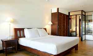 Bild på ett hotellrum med en stor säng med vitt sänglinne, två nattduksbord, bordslampor och skåp i trä. (AI-genererad text)