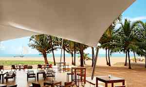 Utomhusservering under ett vitt överdrag med utsikt över sandstrand, palmer och hav. (AI-genererad text)