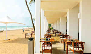 En utomhusterrass med matbord och stolar bredvid en sandstrand. (AI-genererad text)