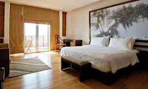 Ett modernt hotellrum med en stor säng, skrivbord, stol och en stor glasdörr som leder till en balkong. (AI-genererad text)