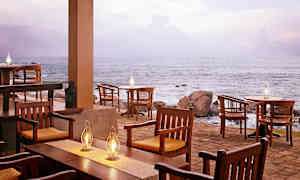 En uteservering vid havet med trästolar och bord, och flera fotogenlampor som lyser. (AI-genererad text)