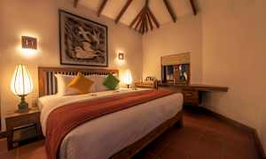 Ett rum med en stor säng, prydd med färgglada kuddar och en röd filt. Det finns en upplyst lampa på sängbordet och ett dekorativt konstverk hänger ovanför sängen. (AI-genererad text)