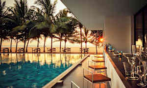 En uteservering vid en pool med utsikt över stranden och palmer vid solnedgång. (AI-genererad text)