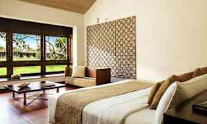 Modernt inrett hotellrum med säng, soffmöbel och stora fönster som vetter mot en grönskande trädgård. (AI-genererad text)