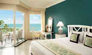 Hotellrum med havsutsikt, inrett med en stor säng, skrivbord, stol och terrassmöbler. (AI-genererad text)