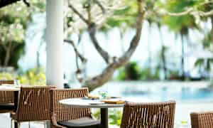 Ett dukat bord med stolar utomhus vid en pool, omgiven av träd och växtlighet. (AI-genererad text)