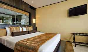 Ett hotellrum med en dubbelsäng, prydd med bruna och gyllene prydnader. En TV hänger på väggen till höger. (AI-genererad text)