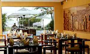 En restaurang med dukade bord och en fönstervy mot en utomhusmiljö med parasoller och grönska. (AI-genererad text)