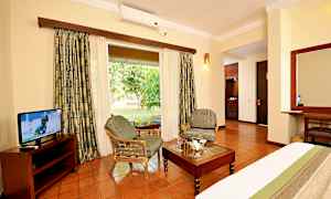 Ett hotellrum med sittmöbler, bord och tv, med en utsikt mot en grön trädgård. (AI-genererad text)