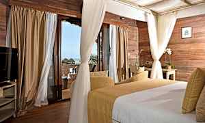 Ett sovrum med träpaneler på väggarna, stora fönster med gardiner och utsikt mot havet. I rummet finns en säng och en sittgrupp. (AI-genererad text)