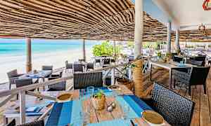 Uteservering med tak av flätad bast vid en sandstrand och blått hav. (AI-genererad text)