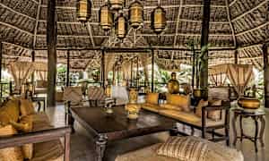 Ett möblerat och dekorerat öppet område med träbord, soffor och lyktor under ett vackert halmtak. (AI-genererad text)