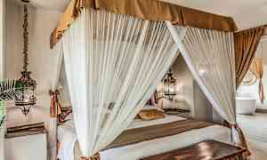 Sovrum med en himmelssäng omsluten av vita gardiner och dekorerad med varma tonade textilier. (AI-genererad text)