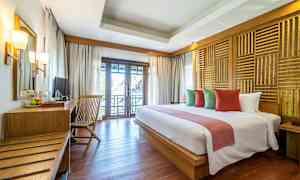 Ett hotellrum med en dubbelsäng, kuddar i olika färger, en träbord med stol samt en balkong med utsikt. (AI-genererad text)