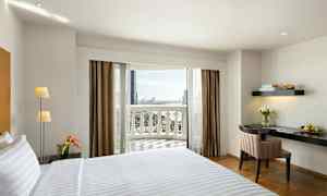 Hotellrum med en bäddad säng, skrivbord och några blommor, samt en balkong med utsikt. (AI-genererad text)