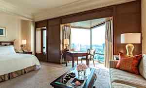 Ett elegant hotellrum med en stor säng, en soffa, ett skrivbord och stora fönster med utsikt över staden. (AI-genererad text)