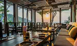 Interiör av en restaurang med dukade bord och stora fönster som släpper in ljus från solnedgången. (AI-genererad text)