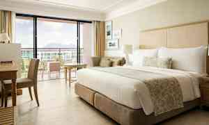 Ett hotellrum med en stor säng, skrivbord, och en balkong med utsikt. (AI-genererad text)