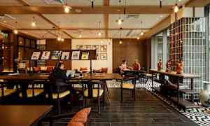 En interiör av ett kafé eller arbetsrum med trämöbler, dekorationer på bordet och människor som arbetar eller samtalar. (AI-genererad text)