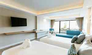 Interiör av ett hotellrum med två bäddade sängar, en väggmonterad TV och ett område med sittmöbler med utsikt mot en balkong. (AI-genererad text)