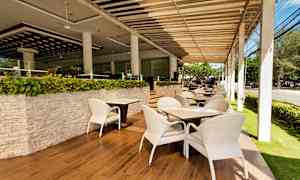 En utomhusrestaurang med vita stolar och bord på ett parkettgolv, omgiven av gröna växter. (AI-genererad text)