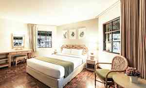 Ett hotellrum med en stor säng, två lampor, ett skrivbord och en stol bredvid ett bord med en blomma. (AI-genererad text)