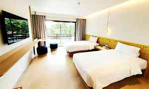 Ett hotellrum med två enkelsängar, en platt-TV på väggen och en balkong med utsikt över grönska. (AI-genererad text)