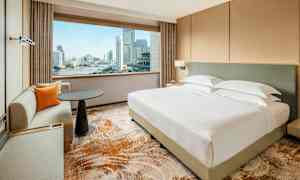 Ett modernt hotellrum med en stor säng och en sittgrupp. Genom fönstret syns en stadsvy och en flod. (AI-genererad text)