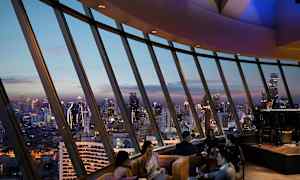 Folk sitter i en lyxig lounge med panoramavy över stadens skyline vid skymning. (AI-genererad text)