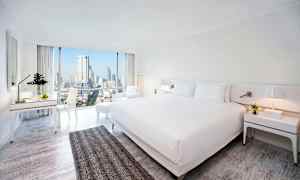 Hotellrum med modern inredning, stor säng och utsikt över stadssilhuetten genom stora fönster. (AI-genererad text)