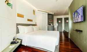 Ett modernt hotellrum med en stor säng, vita sängkläder och träparkettgolv. En TV är monterad på väggen mittemot sängen och det finns en minibar samt en garderob i rummet. (AI-genererad text)