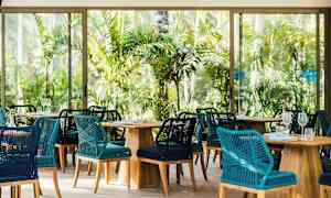 Restaurang med flätade stolar och bord i trä omgiven av tropisk grönska. (AI-genererad text)