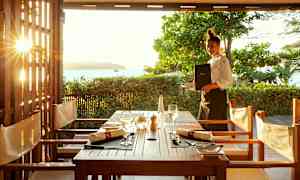 Utsikt över ett dukat bord i en utomhusrestaurang med solnedgång i bakgrunden. (AI-genererad text)