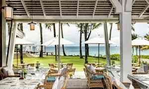 Restaurang med sittplatser och utsikt över en grön gräsmatta, paraplyer och havet. (AI-genererad text)