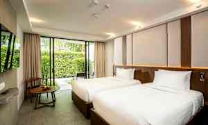 Ett hotellrum med två enkelsängar med vita sängkläder, ett fönster med utsikt över en trädgård och ett träbord med en stol bredvid. (AI-genererad text)