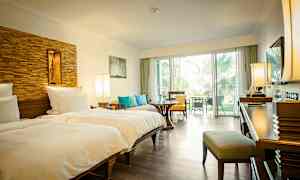Hotellrum med två enkelsängar, sittplats och utsikt mot en grönskande utomhusmiljö. (AI-genererad text)