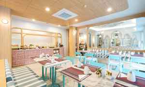 Ett ljust och modernt frukostområde med bord, blå stolar och bufféområde. (AI-genererad text)