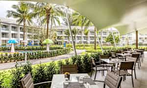 Restaurang med uteservering vid en trädgård med grönytor och lekområde. (AI-genererad text)