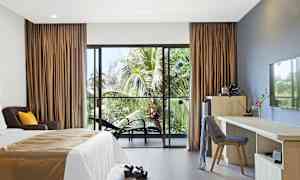 Hotellrum med en säng, skrivbord och stolar, samt utsikt mot palmer genom en glasdörr. (AI-genererad text)