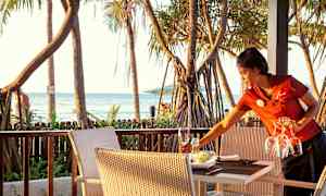 En terrass med bord och stolar, palmer och havet i bakgrunden. (AI-genererad text)