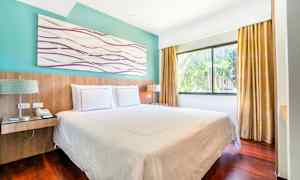 Ett hotellrum med en dubbelsäng, stora fönster och gardiner. (AI-genererad text)