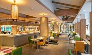 Interiör av en restaurang med bord och stolar i olika färger samt hängande lampor. (AI-genererad text)