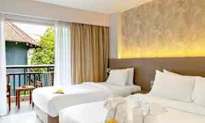 Två bäddade enkelsängar med prydnadshanddukar och blommor. Utsikt mot en möblerad balkong med grönska och byggnad. (AI-genererad text)