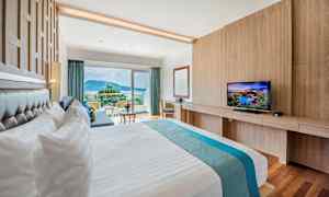 Ett hotellrum med en stor säng, en TV och en balkong med utsikt över omgivningen. (AI-genererad text)