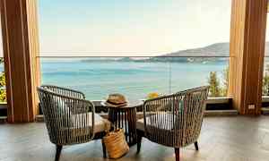 Två stolar och ett bord står på en terrass med utsikt över havet och en bergskust. (AI-genererad text)