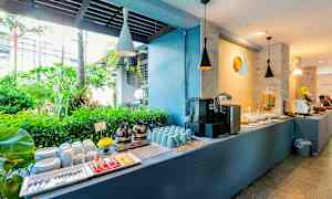 Buffébord med kaffe, koppar, tallrikar och tropisk grönska i bakgrunden. (AI-genererad text)