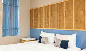 Ett sovrum med en säng, kuddar och en blå vägg med flätade paneler. (AI-genererad text)