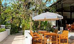 Trädgårdsmöbler under en randig parasoll i en grönskande miljö. (AI-genererad text)