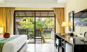 Ett hotellrum med en säng, skrivbord och en balkong med utsikt över trädgård. (AI-genererad text)