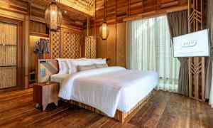 Ett sovrum med en dubbelsäng bäddad med vit sängkläder, träväggar och trägolv. En TV är monterad på väggen. (AI-genererad text)